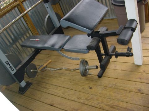 1996 Ford Bronco - A weight bench and barbell are set up on a wooden deck, with corrugated metal siding in the background.