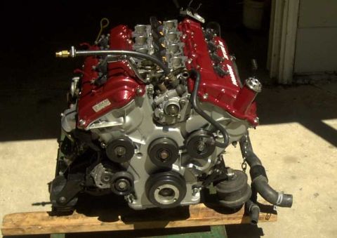 1997 Ford Taurus - Front view of a bare DOHC V6 engine sitting on a wooden dolly outside a garage, with red-painted valve covers and intake plenums over a sil…