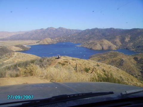 1990 Ford Bronco - A white SUV navigates a dirt road with a scenic view of a lake and mountains under a clear blue sky.