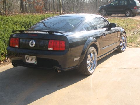 2007 Ford Mustang - Rear three-quarter view of a black 2007 Ford Mustang coupe, custom chrome wheels and a rear spoiler. Another vehicle is visible in the back…