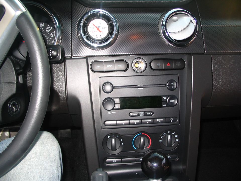 Car dashboard with steering wheel, gauges, radio, and climate controls. A "SUPERMOTORS" watermark is visible