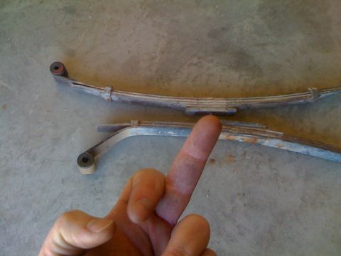 1966 Ford Bronco - Leaf springs are shown on a concrete surface, with a finger indicating a specific point on one of them.