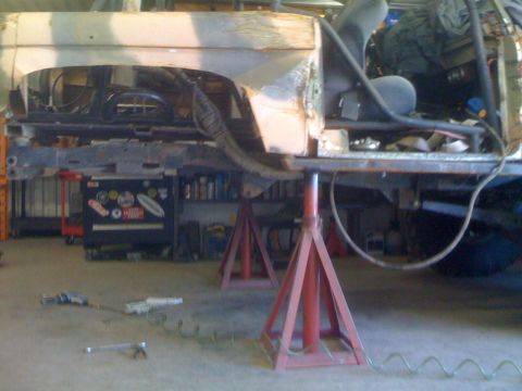 1966 Ford Bronco - The frame of a vehicle is elevated on jack stands in a workshop, revealing its interior and suspension components.