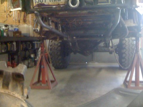 1966 Ford Bronco - The underside of a vehicle is viewed from below, supported by red jack stands in a garage setting.