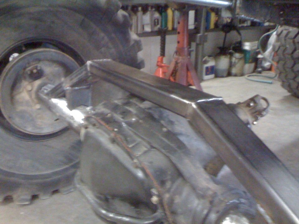 Close-up of a custom suspension component welded onto a vehicle's rear axle, with a large tire visible