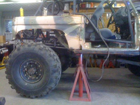 1966 Ford Bronco - This heavily modified vehicle is in a workshop, supported by jack stands and showing its custom roll cage and large off-road tires.