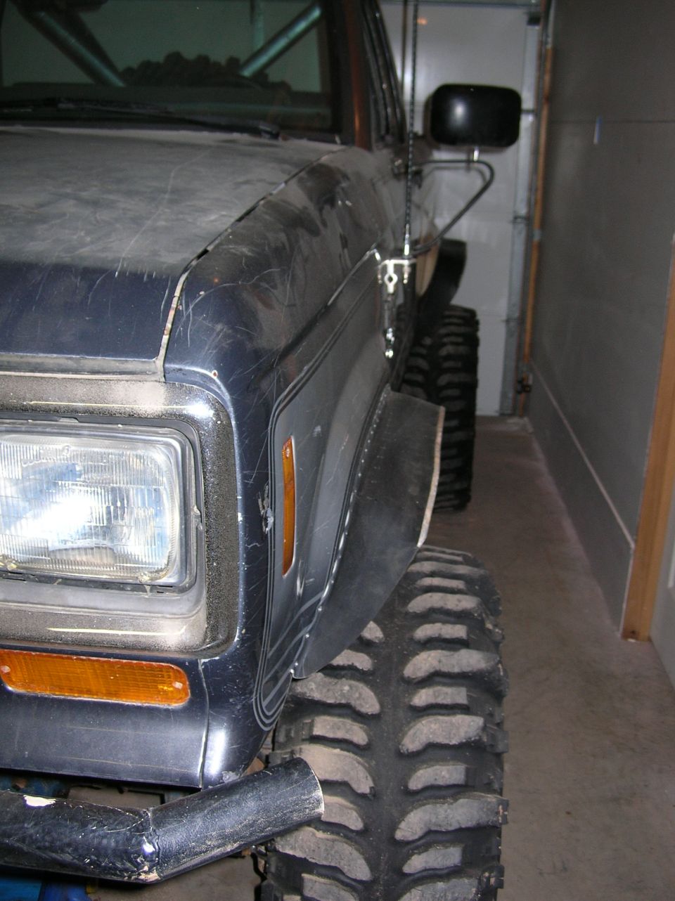 Front corner of a dark blue lifted SUV with tube bumper and mud tires in garage