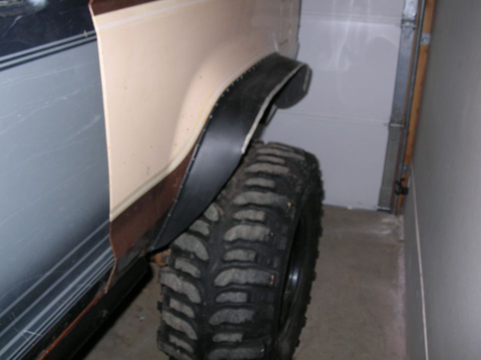 Wide black flare on a trimmed rear wheel opening above a mud tire, seen in a garage