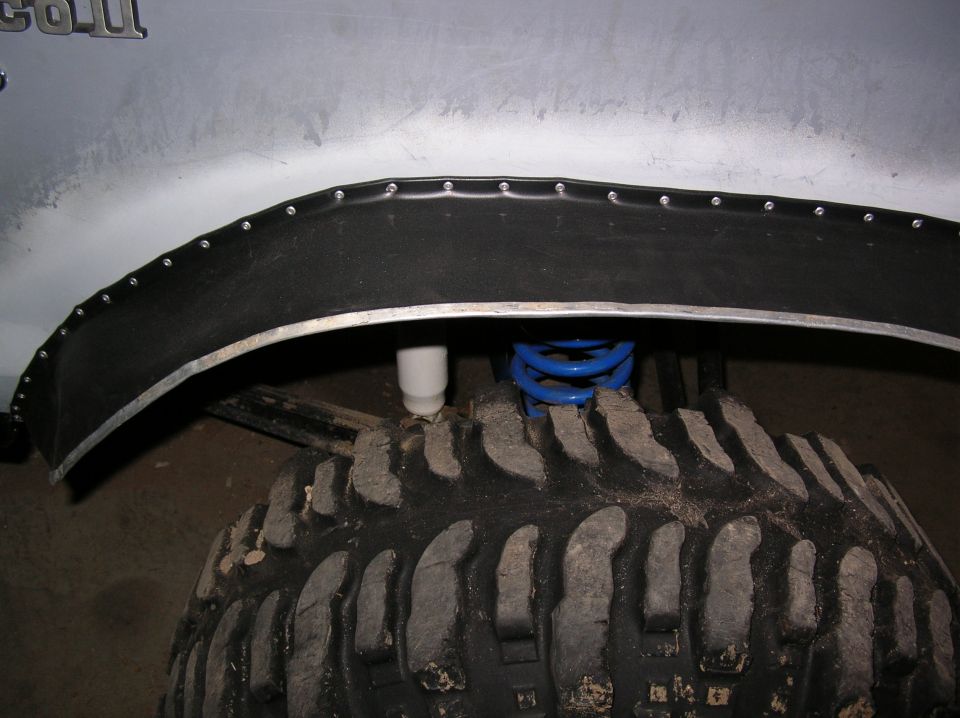 Riveted black rubber fender flare on cut wheel arch above mud tire and blue coil