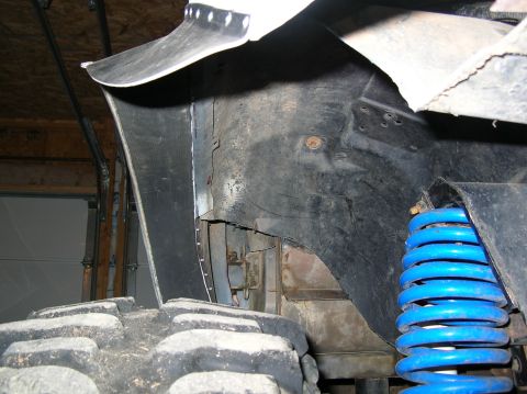 1985 Ford Bronco II - Detail of a vehicle's suspension and wheel well, showing a blue coil spring and part of a large tire.