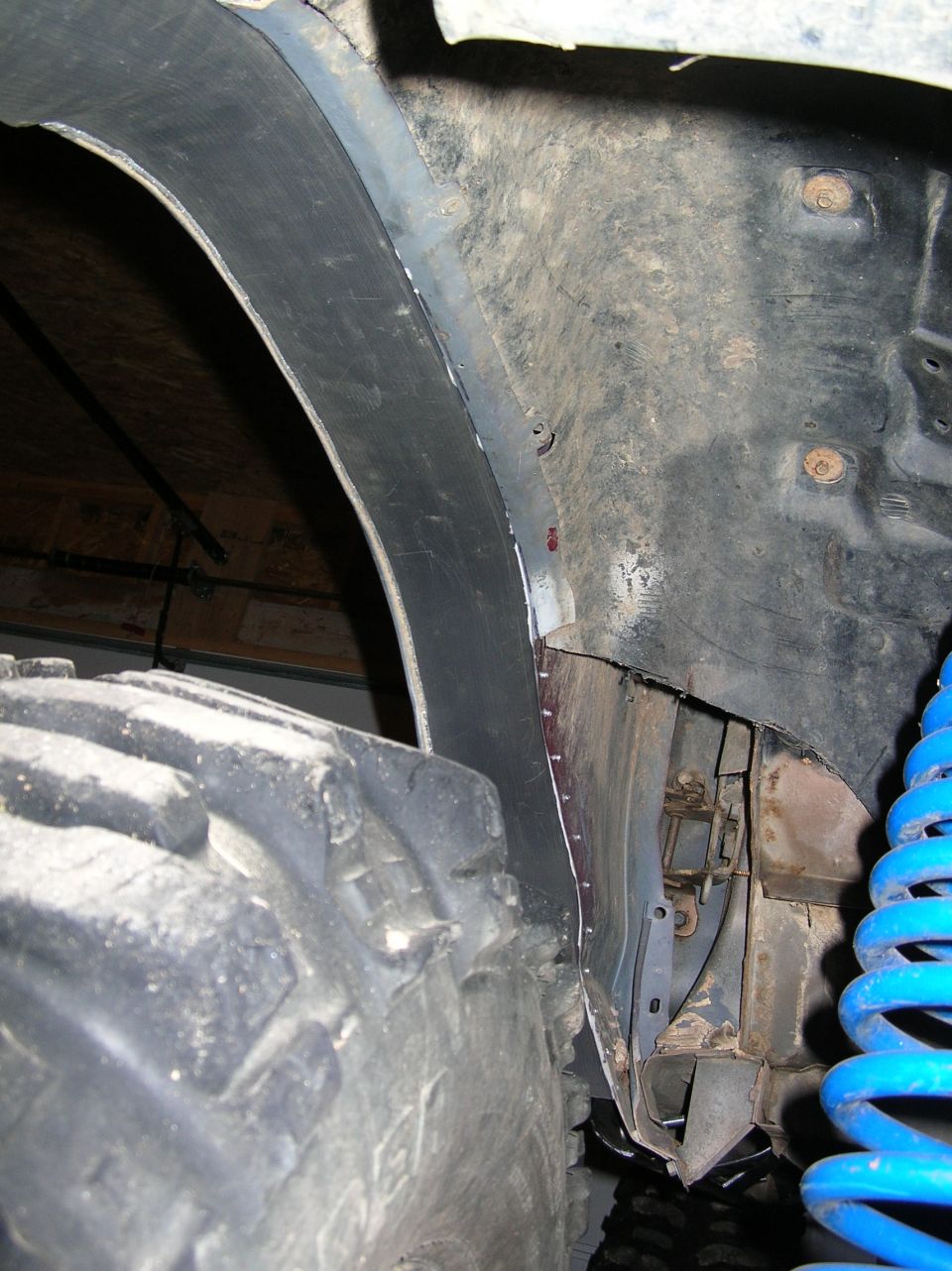 Inner wheel well with mud terrain tire and blue coil spring on a lifted off-road vehicle