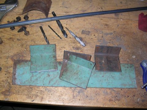 1985 Ford Bronco II - Various metal pieces, some with green paint, and tools like drill bits and a wrench are laid out on a workbench.