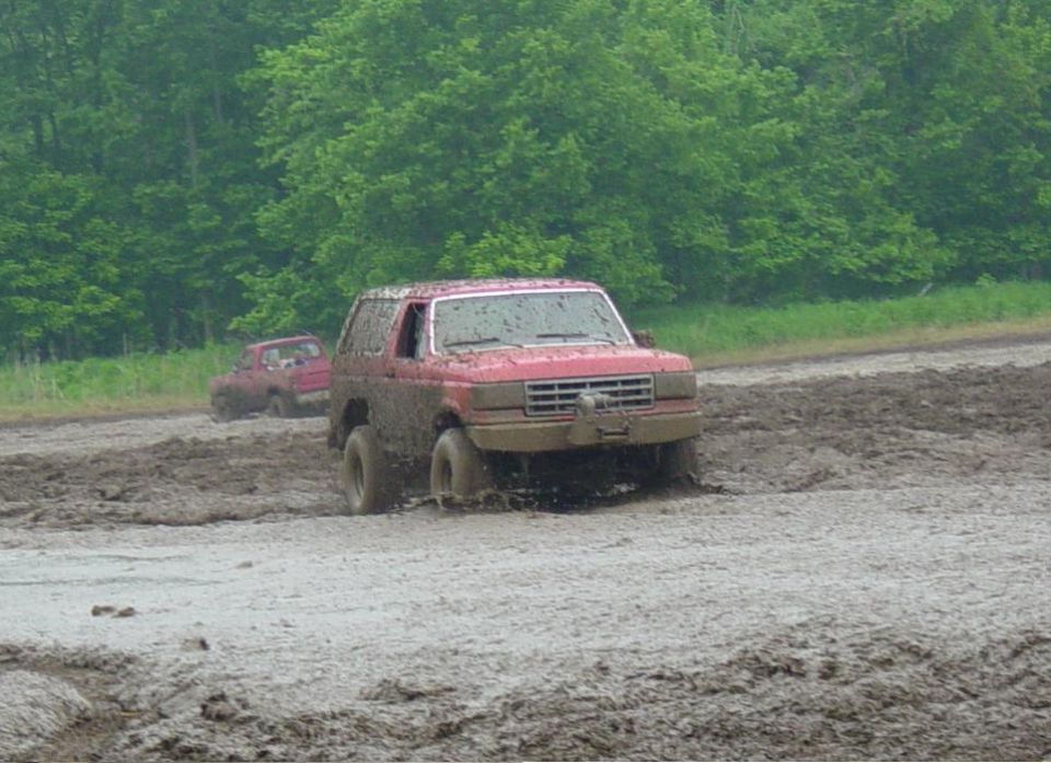 Red Ford Bronco churning through deep mud at an off-road mud park