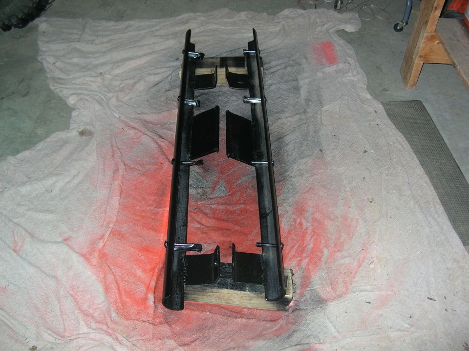 Pair of freshly painted black tube rock sliders with mounting plates on a garage drop cloth