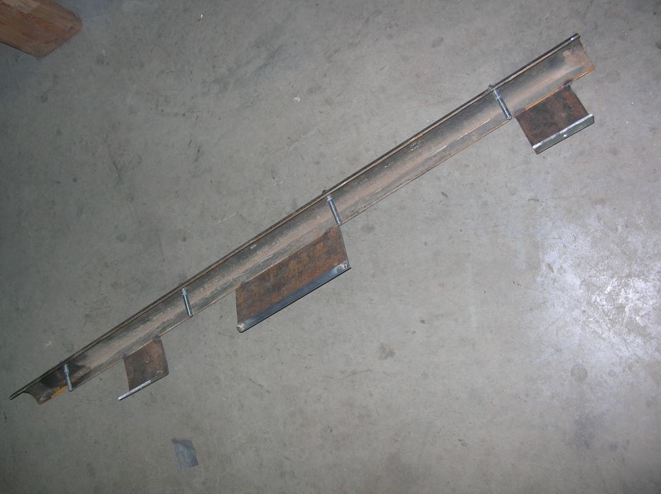 Bare steel tube rock slider with angle iron and three mounting brackets on a concrete floor