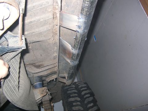 1985 Ford Bronco II - Close-up view of the underbody of a vehicle, focusing on the tire, exhaust system, and what appears to be repair work on a pipe.