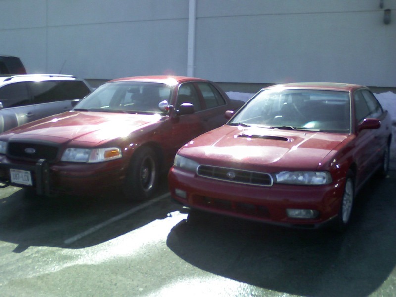 Red Subaru Legacy sedan parked beside a red Ford Crown Victoria
