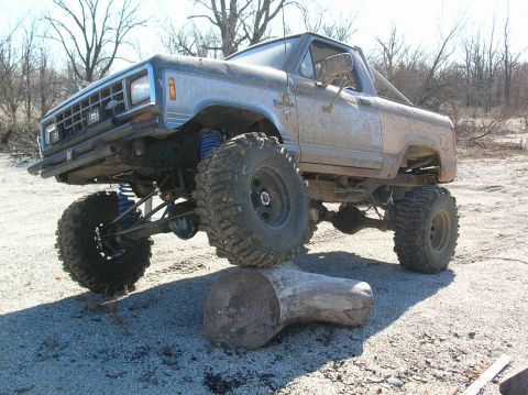 1985 Ford Bronco II - A heavily modified SUV navigates an obstacle with its front tire resting on a log.