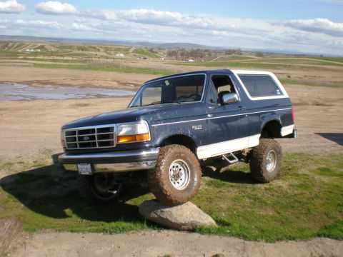 1993 Ford Bronco - A lifted Ford Bronco is shown in a rural landscape with one tire resting on a large rock.