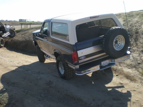 1993 Ford Bronco - This Ford Bronco is shown from the rear on a dirt path, with another vehicle on an incline in the background.