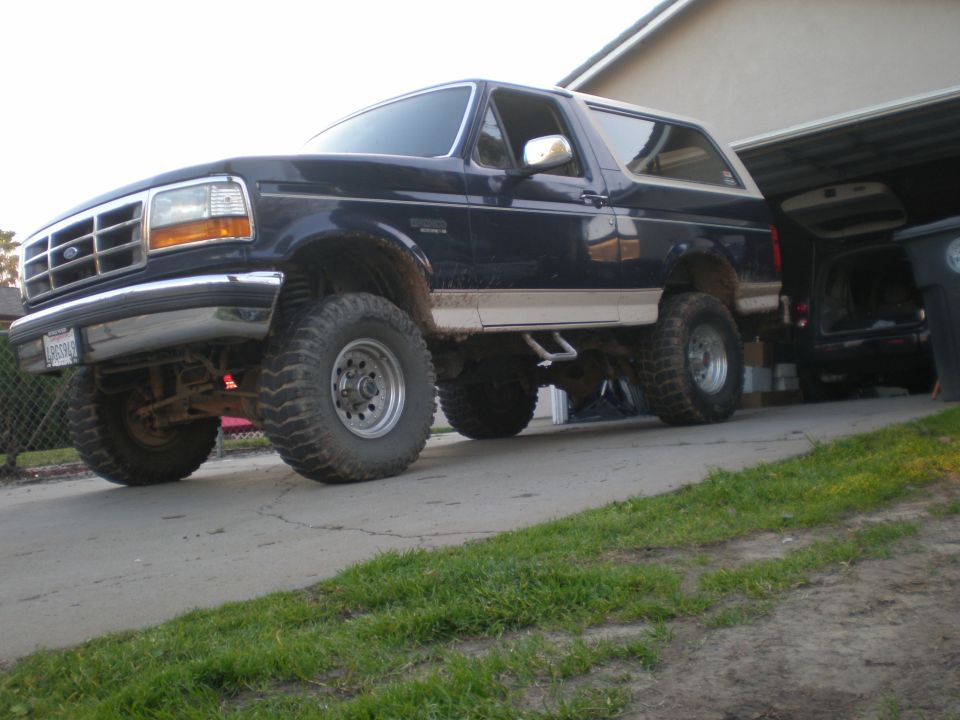 Dark blue Ford Bronco with lifted suspension and large tires parked in a driveway