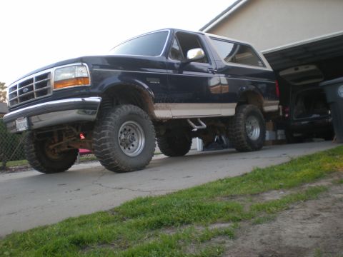 1993 Ford Bronco - This dark blue 1993 Ford Bronco features a lifted suspension and aggressive off-road tires, parked in a driveway next to another vehicle.
