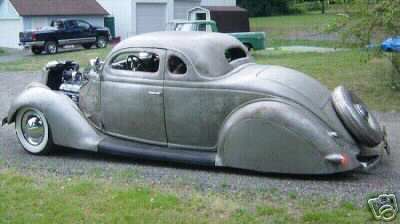 1936 Ford Coupe - This 1936 Ford Coupe hot rod features a patina finish and an exposed engine, viewed from the front three-quarter angle.