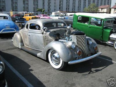 1936 Ford Coupe - A custom 1936 Ford Coupe hot rod with its hood open sits in a parking lot with other vehicles.