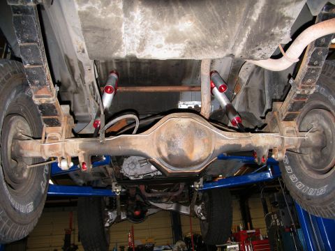 1984 Ford Bronco - The rear suspension and axle assembly of a vehicle are visible from below while it is elevated on a lift.