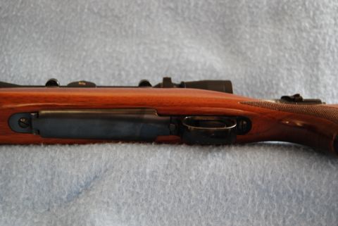 1991 Ford Bronco - Close-up of a rifle's action, trigger, and scope, set against a blue textured background.
