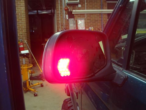 1996 Ford Bronco - The back of a black side mirror on a dark blue truck glows red from a cluster of bright LEDs mounted inside the empty mirror shell, mid-fit…