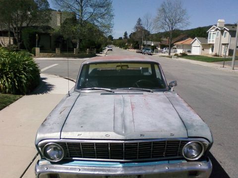 1964 Ford Ranchero - A 1964 Ford Ranchero sits parked on a suburban street, its paint showing significant wear.