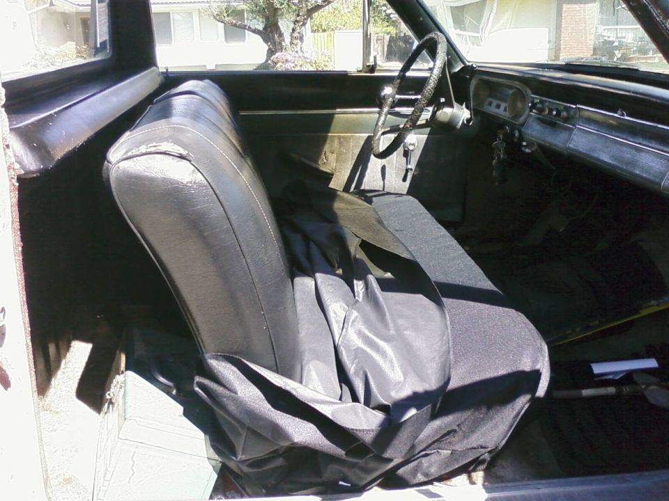 Interior of a car, showing the driver's seat and dashboard. A black cover is on the passenger seat
