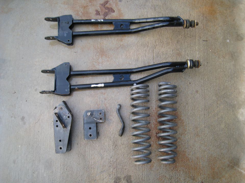 Two black control arms and two coil springs on concrete
