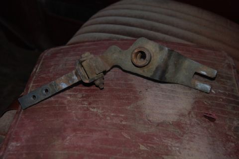 1987 Ford F-250 - A close-up view of a rusty metal linkage part, likely from a vehicle's transfer case shifter, resting on a red, textured surface.