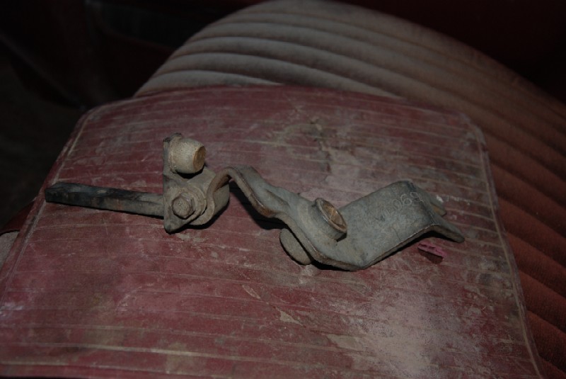 Transfer case shifter linkage part on a red surface, with ribbed upholstery in the background