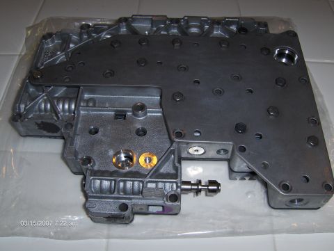 2004 Ford Crown Victoria - A metal valve body part is shown, with visible ports and fasteners.
