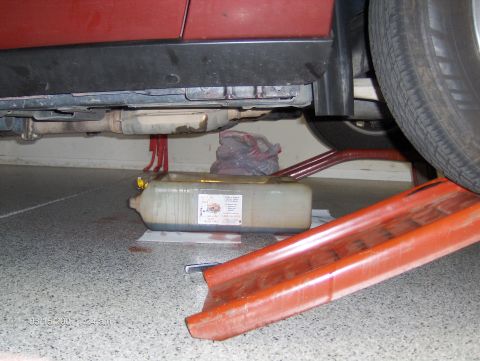 2004 Ford Crown Victoria - A red car's undercarriage is shown with an oil drain pan positioned to catch fluid.