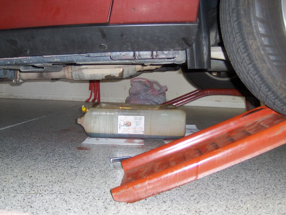Red car's undercarriage with exhaust pipe and oil drain pan on the ground
