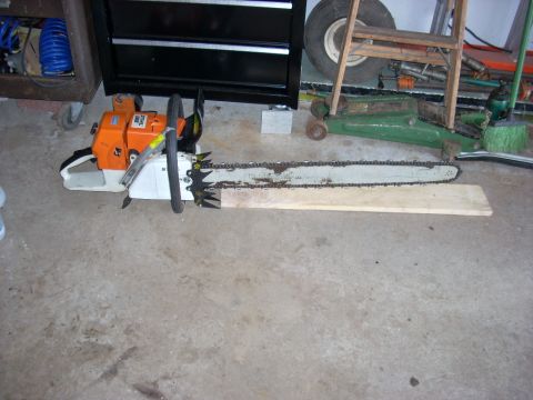2000 Chevrolet Tahoe - A chainsaw rests on a concrete floor, with a wooden plank positioned along its bar. Other tools and equipment are visible in the background.