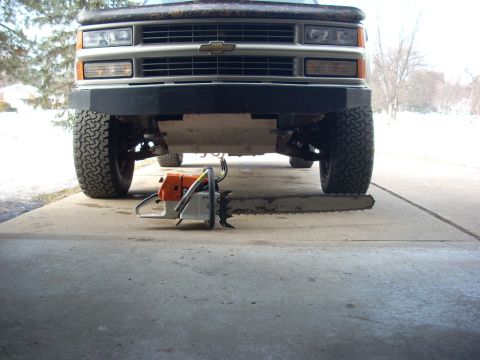 2000 Chevrolet Tahoe - A chainsaw lies on the ground in front of a 1995 Chevrolet pickup truck, suggesting a humorous or unusual situation.
