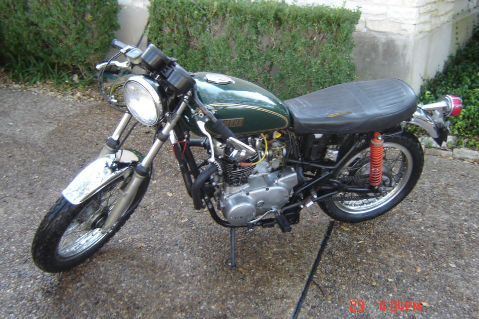 Green motorcycle parked on a driveway. It has a black seat and chrome fenders