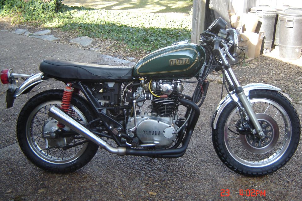 Green Yamaha motorcycle with chrome exhaust and red rear shocks, seen from the side