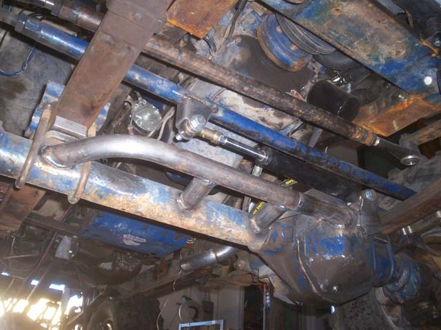 Underside view of a vehicle's suspension and steering linkage, showing heavy-duty components and blue-painted axle housing