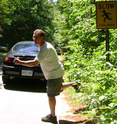 1997 Ford Taurus - A man points at the rear of a black 1997 Ford Taurus parked on a roadside next to a 'Slow Children' sign.