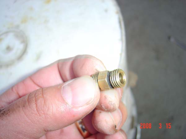 Hand holding a brass fitting with threaded ends and a black O-ring