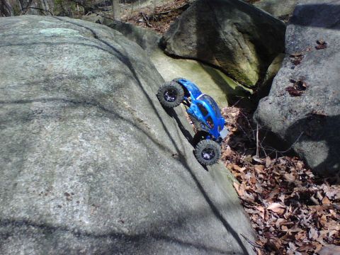 1996 Ford Bronco - A blue remote control rock crawler navigates a steep, rocky incline in a wooded area.