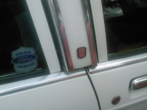 1991 Ford Crown Victoria - Close-up of a white car's side door, showing chrome trim and a 'Ford Police Vehicles' sticker.