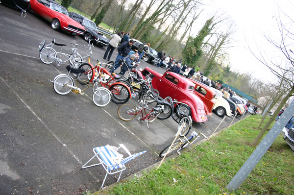 Several vintage cars and bicycles parked in a lot, with people milling around