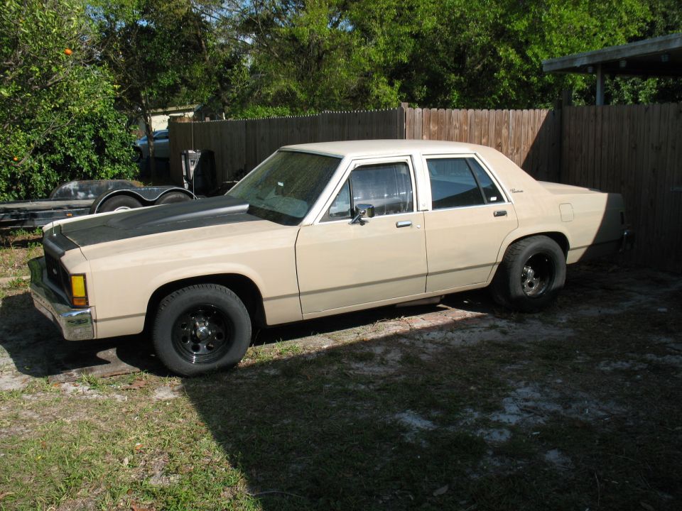 Tan sedan with a black hood and black wheels parked in a yard